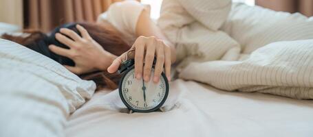 alarm clock and asian woman hand stop time in bed while sleeping, young adult female wake up late in the early morning. Relaxing , sleepy, daily routine and have a nice day concepts photo