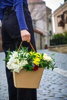 Person Holding Basket of Flowers on Cobblestone Street photo