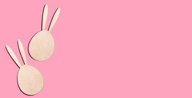 Easter background with wooden rabbits on a pink background. Easter card. Copy space. Banner. photo