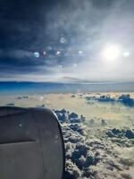 View from an airplane window of the sun and great cloud formations with many small spots on the window. photo