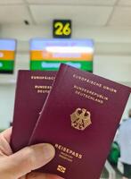 un mano sostiene dos alemán pasaportes en frente de un suave viaje aeropuerto antecedentes en vacaciones. foto