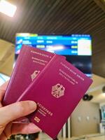 un mano sostiene dos alemán pasaportes en frente de un suave viaje aeropuerto antecedentes en vacaciones. foto