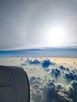 View from an airplane window of the sun and great cloud formations with many small spots on the window. photo