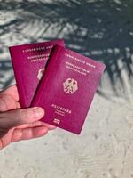 un mano sostiene dos alemán pasaportes en frente de un suave viaje antecedentes en el Maldivas con palma arboles y playa. foto