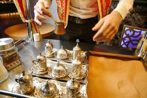 Man Standing Over Table With Silver Cups and Saucers photo