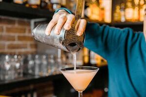 Bartender Pours a Drink Into a Martini Glass at a Lively Bar Counter photo