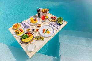 desayuno en piscina, desayuno flotante en lujoso resort tropical. mesa para relajarse en el agua tranquila de la piscina, desayuno saludable y plato de frutas junto a la piscina del centro turístico. pareja tropical playa estilo de vida de lujo foto