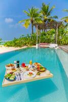 desayuno en piscina, desayuno flotante en lujoso resort tropical. mesa para relajarse en el agua tranquila de la piscina, desayuno saludable y plato de frutas junto a la piscina del centro turístico. pareja tropical playa estilo de vida de lujo foto