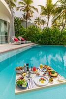 Breakfast in swimming pool, floating breakfast in luxurious tropical resort. Table relaxing on calm pool water, healthy breakfast and fruit plate by resort pool. Tropical couple beach luxury lifestyle photo