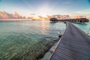 Amazing beach panoramic landscape. Beautiful Maldives sunset seascape view. Horizon colorful sea sky clouds, over water villa pier pathway. Tranquil island lagoon, vacation travel panorama background photo