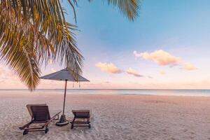 Beautiful tropical sunset scenery, two sun beds, loungers, umbrella under palm tree. White sand, sea view with horizon, colorful twilight sky, calmness and relaxation. Inspirational beach resort hotel photo