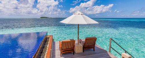 Luxury beach resort, bungalow near endless pool over beautiful blue sea. Amazing tropical island, summer vacation concept. Couple chairs with umbrella, perfect summer leisure vacation holiday panorama photo