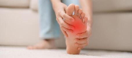 mujer teniendo descalzo dolor durante sentado en sofá a hogar. pie dolor debido a plantar fascitis y despertar largo tiempo. salud y médico concepto foto