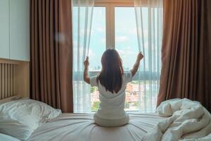happy woman stretching on bed after wake up, young adult female rising arms and looking to window in the early morning. fresh relax and have a nice day concepts photo