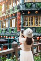 woman traveler visiting in Taiwan, Tourist taking photo and sightseeing in Jiufen Old Street village with Tea House background. landmark and popular attractions near Taipei city. Travel concept