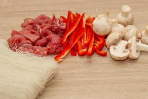 Sliced meat, mushrooms and red pepper on a board with rice glass noodles Funchoza. photo