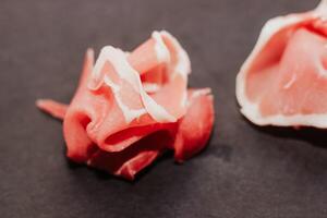 Pieces of dried pork jamon prosciutto on a black board. photo