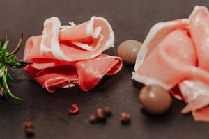 Pieces of dried pork jamon prosciutto with olives on a black board. photo