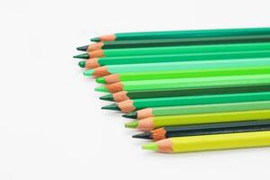 Multi-colored pencils lie on a white table, the green range of colors photo