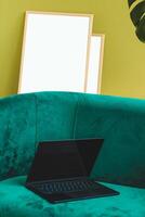 A thin laptop working computer stands on a stylish green sofa in the interior. photo