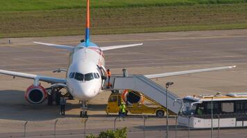 sotsji, Rusland - augustus 02, 2022. sukhoi superjet van azimut Aan de schort. vliegtuig onderhoud na landen. passagiers Uitgang via de trap. platform bus aan het wachten voor passagiers video