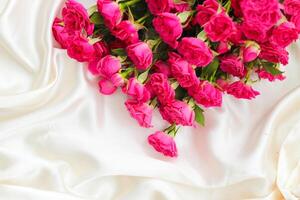 pequeño rosado arbusto rosas en un blanco seda antecedentes con un sitio para texto foto