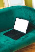 A thin laptop working computer stands on a stylish green sofa in the interior. photo