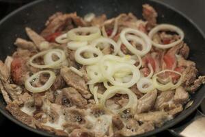 Chopped pieces of pork are fried in a pan with onions cut into rings. photo