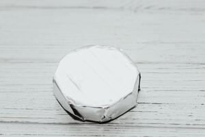 Camembert cheese wrapped in a package with foil on the table. photo