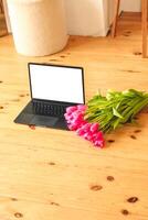 A bouquet of pink tulips flowers on a background of boards with an open laptop. photo