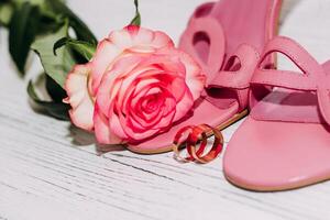 Pink tea rose with wedding rings and shoes on wooden white boards background. photo