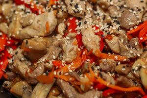 Chopped pieces of pork are fried in a pan with onions, pepper and sesame seeds. photo