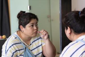 Reflection of Beautiful Asian Plus-size Woman Using Large Mirror to Curl Eyelashes with Curler photo