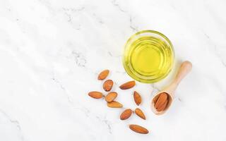 ai generado amarillo almendra petróleo en un claro cuenco con un de madera cuchara siguiente a eso y varios Almendras en un blanco antecedentes foto