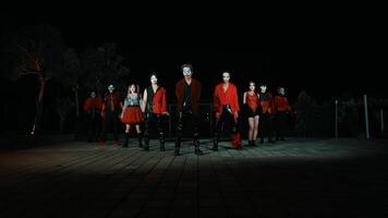 grupo do dançarinos realizando uma rotina às noite com dramático iluminação e vibrante vermelho trajes, exibindo energia e movimento. video