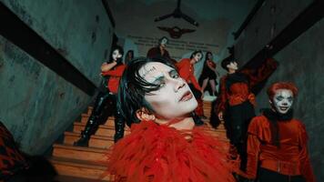 Group of people in red and black with masks descending a staircase in a dimly lit, eerie corridor. video