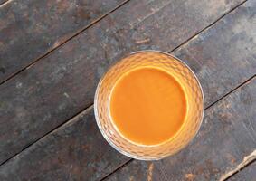 Top view of hot orange or yellow condensed milk tea in transparent glass on old wooden table photo