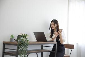 un japonés mujer comprobación teléfono inteligente por remoto trabajo en el hogar oficina foto