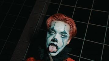 une homme dans une rouge costume et pitre maquillage des rires tandis que posant dans une très terrifiant pose, pendant Halloween video