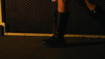 Close-up of a woman's legs in a red skirt and black boots sitting on a bench with a dark, moody background. video