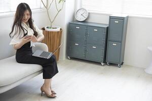 un japonés mujer comprobación teléfono inteligente por remoto trabajo en el hogar oficina foto