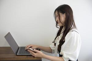 un japonés mujer comprobación teléfono inteligente por remoto trabajo en el pequeño oficina foto