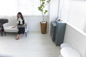 un japonés mujer comprobación teléfono inteligente por remoto trabajo en el pequeño oficina foto