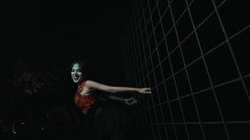 Person in a mask and costume leaning against a metal grid at night, creating a mysterious and dramatic atmosphere. video