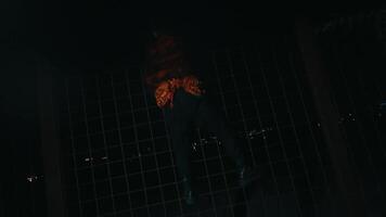 uma homem dentro uma vermelho camisa e palhaço Maquiagem danças dentro frente do a ferro cerca enquanto posando muito assustadoramente às noite. video