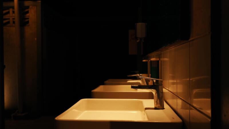 Dimly lit public bathroom with a row of white sinks and mirrors, creating a moody and mysterious atmosphere. 39241668 Stock Video at Vecteezy