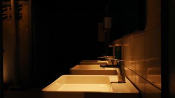 Dimly lit public bathroom with a row of white sinks and mirrors, creating a moody and mysterious atmosphere. video