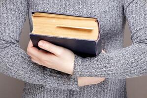 mano de un invisible persona sostiene abrazos un antiguo libro. alto calidad foto