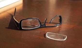 broken eyeglass frame lies on a brown wooden table. High quality photo