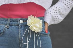 Beautiful white decorative flower on the blue jeans of a young slim woman, close-up. Stylish decorative item. photo